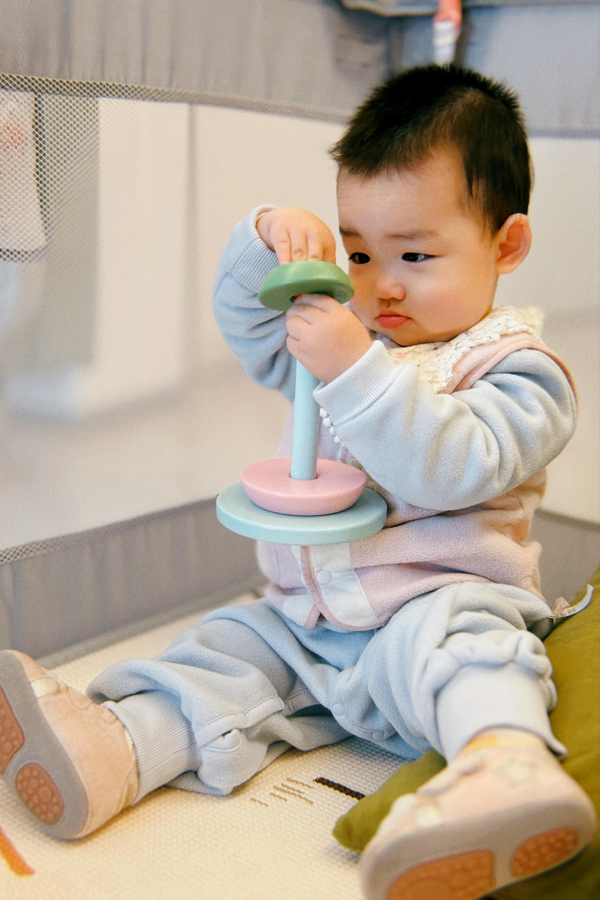 A toddler sits on a countertop, engaged in play with a toy, wearing a blue onesie and looking intently at the object in their hands