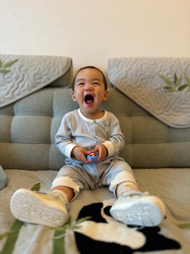 A joyful toddler in pajamas is sitting on a couch, laughing with his mouth wide open