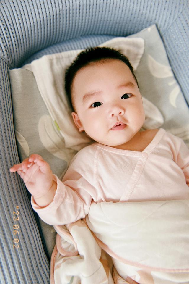 A baby lying on its back, wearing a pink outfit and looking at the camera