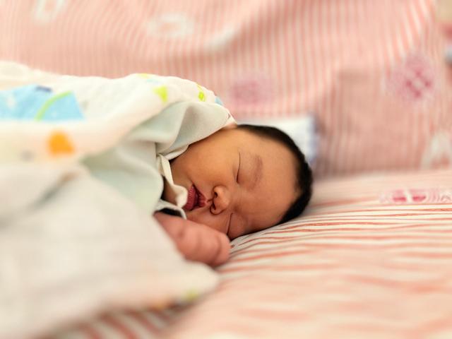 A newborn baby sleeps peacefully on a pink blanket