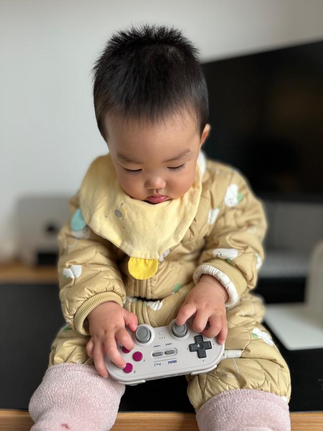 A toddler in yellow pajamas is intently examining a video game controller