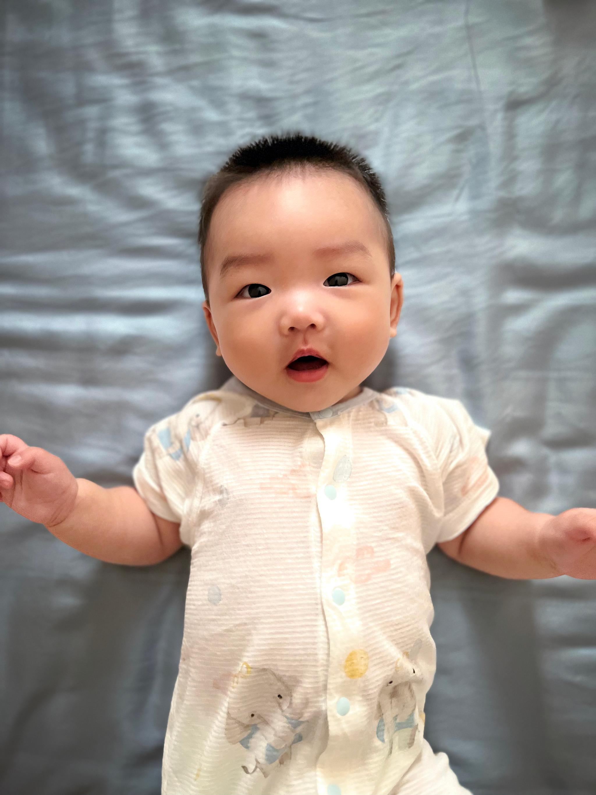 A baby with a surprised expression lies on a textured grey background