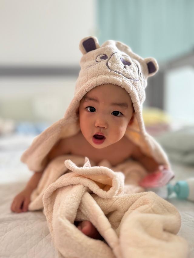 A baby wearing a cute bear hat looks surprised, wrapped snugly in a soft blanket
