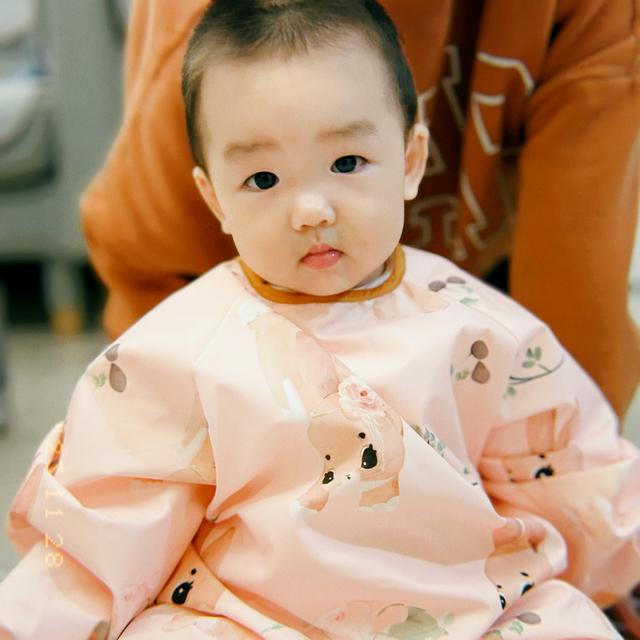 A baby with a serious expression, wearing a pink garment adorned with cartoon bears
