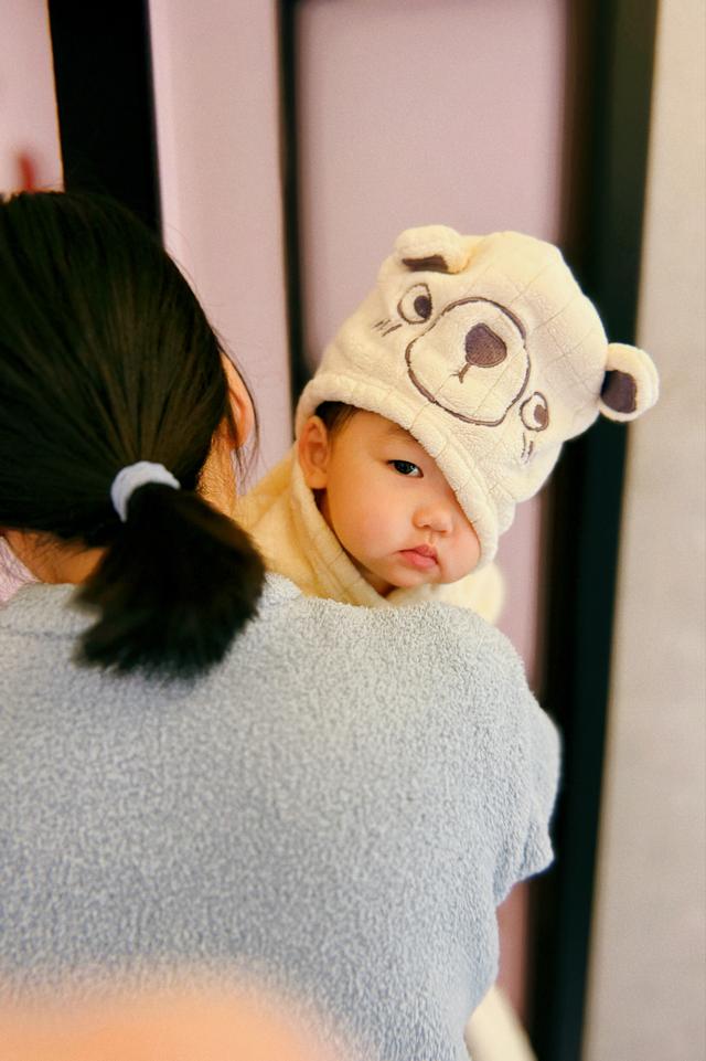 A baby wearing a cute bear hat looks over a person's shoulder, exhibiting a pensive expression