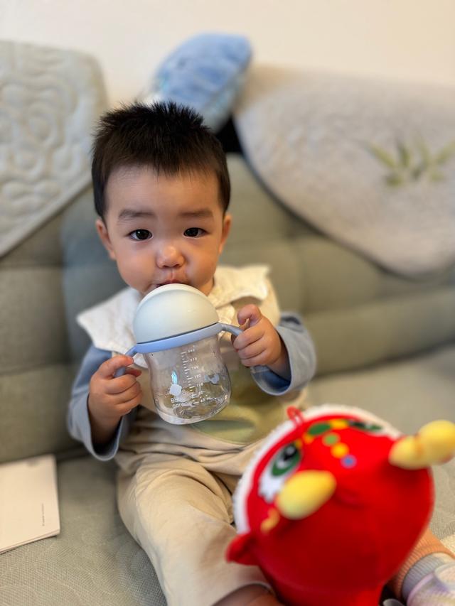 A toddler sits biting a plastic toy, with a red plush toy beside them