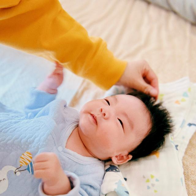 A baby lying on a blanket with someone's hand gently touching the baby's head