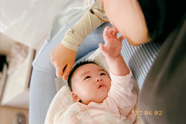 A baby is cradled in an adult's arms, gazing upward, while the adult gently touches the baby's hand