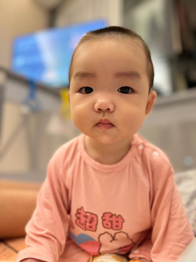 A young child with a solemn expression, wearing a pink top, is captured up-close with a blurred background