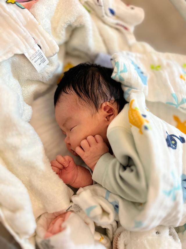 A newborn baby sleeping peacefully, swaddled in a blanket with a pattern of yellow ducks